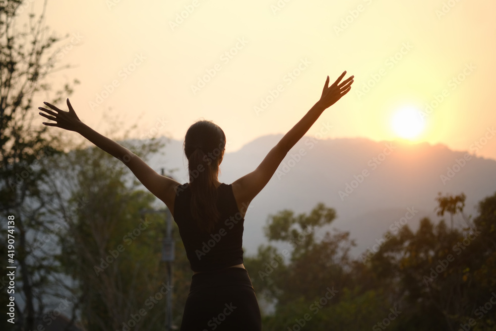 Wall mural young sporty woman cheering and celebrating after evening jogging outdoor at sunset in park.