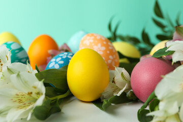 Fototapeta na wymiar Color Easter eggs and alstroemeria flowers against mint background