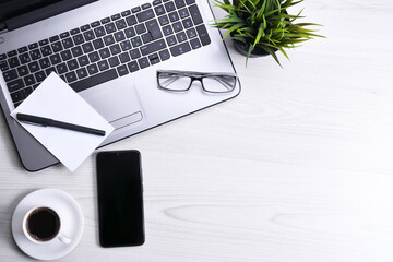 Top view of office work space, wooden desk table with laptop notebook,keyboard ,pen,eyeglasses,phone,notebook and cup of coffee.With copy space, flat lay.Mock up.