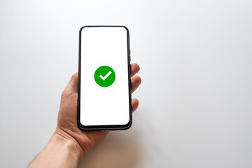 Holding a smartphone with a green checkmark to indicate its approved, approved, completed, or approved status