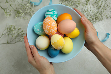 Female hands hold plate of colorful Easter eggs, top view