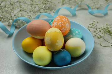 Plate with colorful Easter eggs, ribbon and gypsophila flowers on white textured background