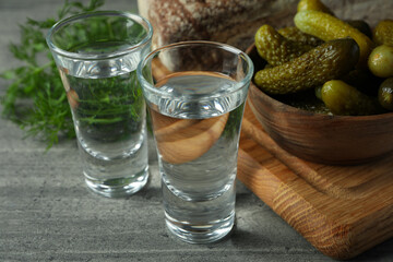Shots of vodka, pickles, bread and dill on gray table