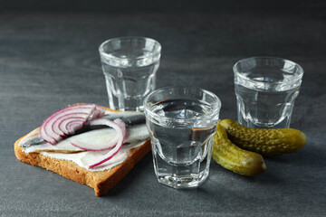 Shots of vodka and tasty snacks on dark wooden background