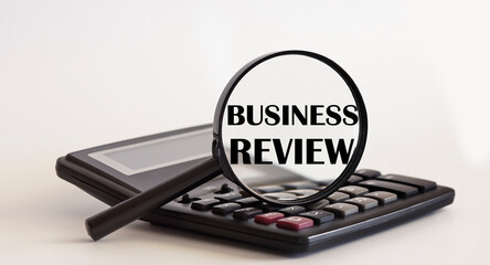 Focused on BUSINESS REVIEW concept. Magnifier glass with text on calculator. Business concept