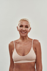 Fototapeta premium Natural beauty. Portrait of a happy caucasian mature woman in underwear smiling at camera while standing against light background