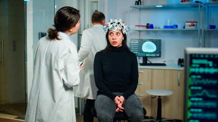 Doctor specialist in neurological medicine typing health informations of patient. Woman wearing eeg headset answering to medical researcher, monitor showing brain scan in equipped laboratory