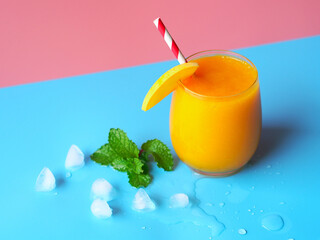 Iced mango smoothies glass on a pink and blue color background for summer party drinks concept.