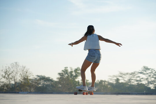  Asian women surf skate or skates board outdoors on beautiful summer day. Happy young women play surf skate at park on morning time.