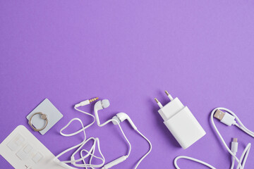 a set of accessories for a smartphone, charger, headphones, holding a ring, adapters for sim cards on a purple background copy space