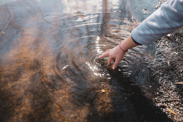 Shallow depth of field (selective focus) details with the hand of a young girl playing with her hand in the shallow water of a lake.