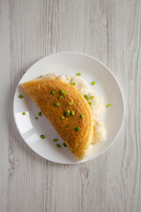 Homemade Fluffy Omelet on a white plate on a white wooden background, top view. Flat lay, overhead, from above.