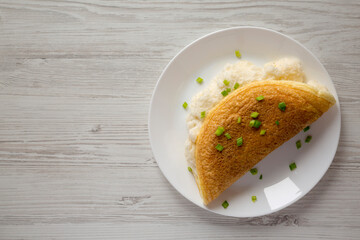 Homemade Fluffy Omelet on a white plate on a white wooden surface, top view. Flat lay, overhead, from above. Copy space.