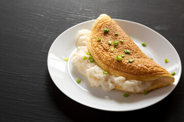 Homemade Fluffy Omelet on a white plate on a black background, side view. Copy space.
