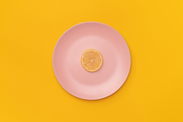 Slice of the fresh lemon on a pink plate. The background is yellow. Minimalism. Minimal cooking concept