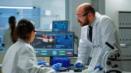 Fototapeta premium Team of scientists worried about virus evolution discussing in equipped laboratory pointing at computer. Stuff examining vaccine development using high tech researching treatment against covid19 virus