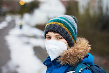 Kid boy wearing ffp medical mask on the way to school. Child backpack satchel. Schoolkid on cold autumn or winter day with warm clothes. Lockdown and quarantine time during corona pandemic disease