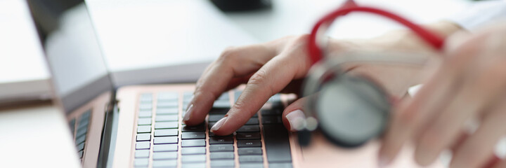 Doctors hands holding stethoscope and typing on keyboard closeup