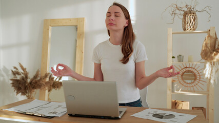 Young woman with closed eyes meditation spread hands in yoga pose sit after work at desk with laptop