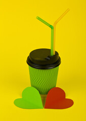 Green paper cup and hearts on a yellow background.
