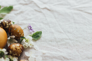 Easter eggs with spring flowers on rustic linen background with space for text. Holiday aesthetic