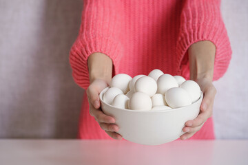 Girl in pink sweater holds white bowl full of eggs. Easter or healthy food concept. No face