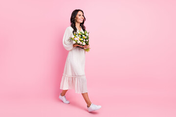 Full size profile side photo of happy young woman walk empty space hold hands flowers weekend isolated on pink color background