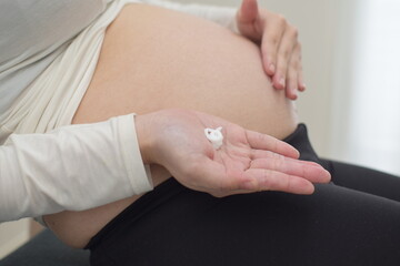 A young pregnant woman sits in a chair and moisturizes her enlarged belly with cream. Moisturizing can prevent stretch marks.