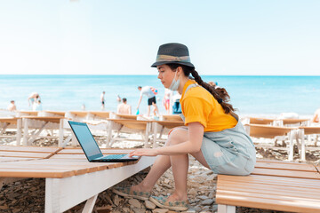Freelance. A woman with a medical mask on her face, sitting on a chaise longue and typing on a...