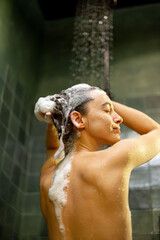Woman staying back in shower apply shampoo with water dripping. Taking shower and relaxing under warm running water. 