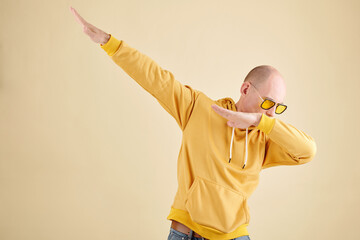 Studio portrait of bald mature man in yellow hoodie making dabbing gesture when enjoying dancing alone