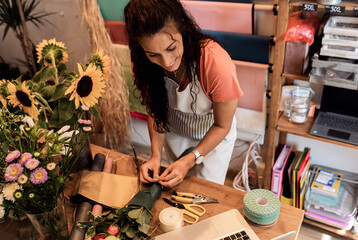 Young woman working in flower shop and making bouquet for customer.	