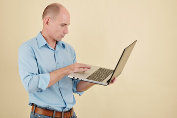 Serious mature software developer pushing button of laptop in his hand and launching new program