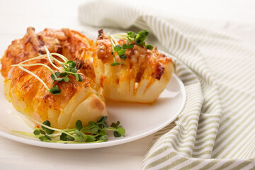 Closeup view of traditional baked potatoes with cheese and bacon topped with radish microgreens in white plate on the table. Healthy homemade food concept, selective focus