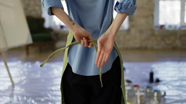 Rare view woman fasten up green apron in art studio