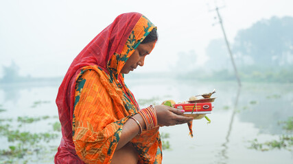 Woman praying holding fruits in hand during chhath puja - obrazy, fototapety, plakaty