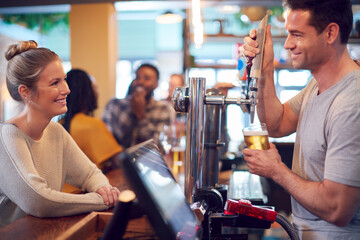 Smiling Male Bartender Behind Counter Serving Female Customer With Beer