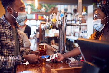 Male Customer Wearing Mask In Bar Making Contactless Payment For Drinks During Health Pandemic