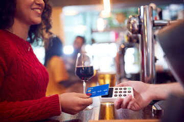 Smiling Female Customer In Bar Making Contactless Payment With Card For Drinks To Male Bartender