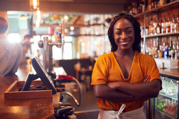 Portrait Of Smiling Female Bar Owner Standing Behind Counter - obrazy, fototapety, plakaty