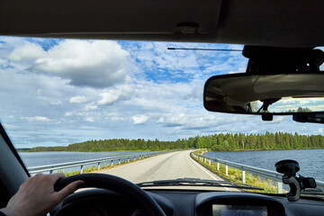 Car salon, steering wheel, hand of woman and view on nature landscape. Road, forest, blue sky, white clouds at sunny day. Concept of single trip of female traveller and driver during coronavirus