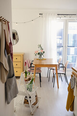 Cozy open dining room and living room interior with a window and a table with chairs. Spring flower decor on a kitchen rolling utility cart. Scandinavian decor concept.