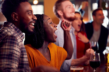 Group Of Excited Customers In Sports Bar Watching Sporting Event On Television