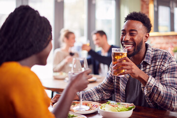 Smiling Young Couple On Date Making Toast Before Enjoying Pizza In Restaurant Together