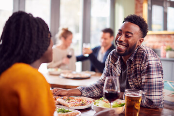 Smiling Young Couple On Date Enjoying Pizza In Restaurant Together