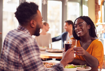 Smiling Young Couple On Date Making Toast Before Enjoying Pizza In Restaurant Together
