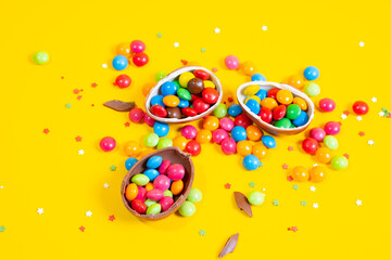 Chocolate Easter eggs with colored candies on a yellow background.