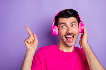 Photo of young happy cheerful excited man in headphones point finger copyspace advertise isolated on violet color background