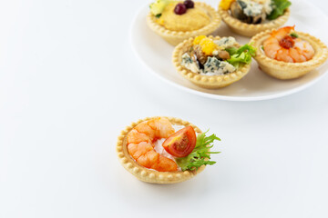 Tartlets with seafood, cheese and herbs on a white table.