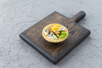 Tartlet with mussels, blue cheese and orange on a wooden board.
